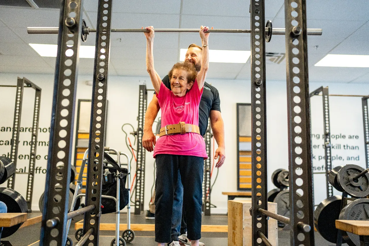 An older woman doing assisted chin-ups with a coach spotting her