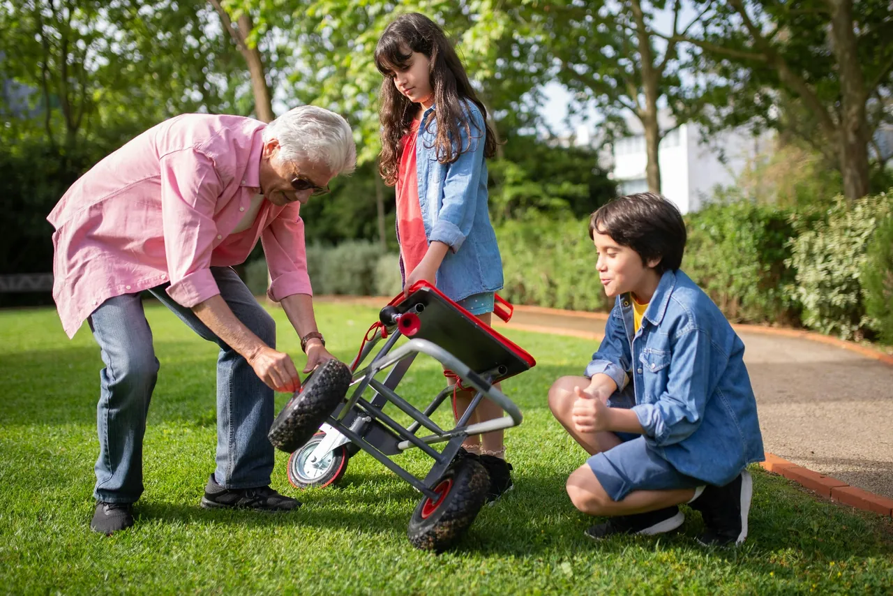 An active older man fixing a cart in the yard with his two grandchildren