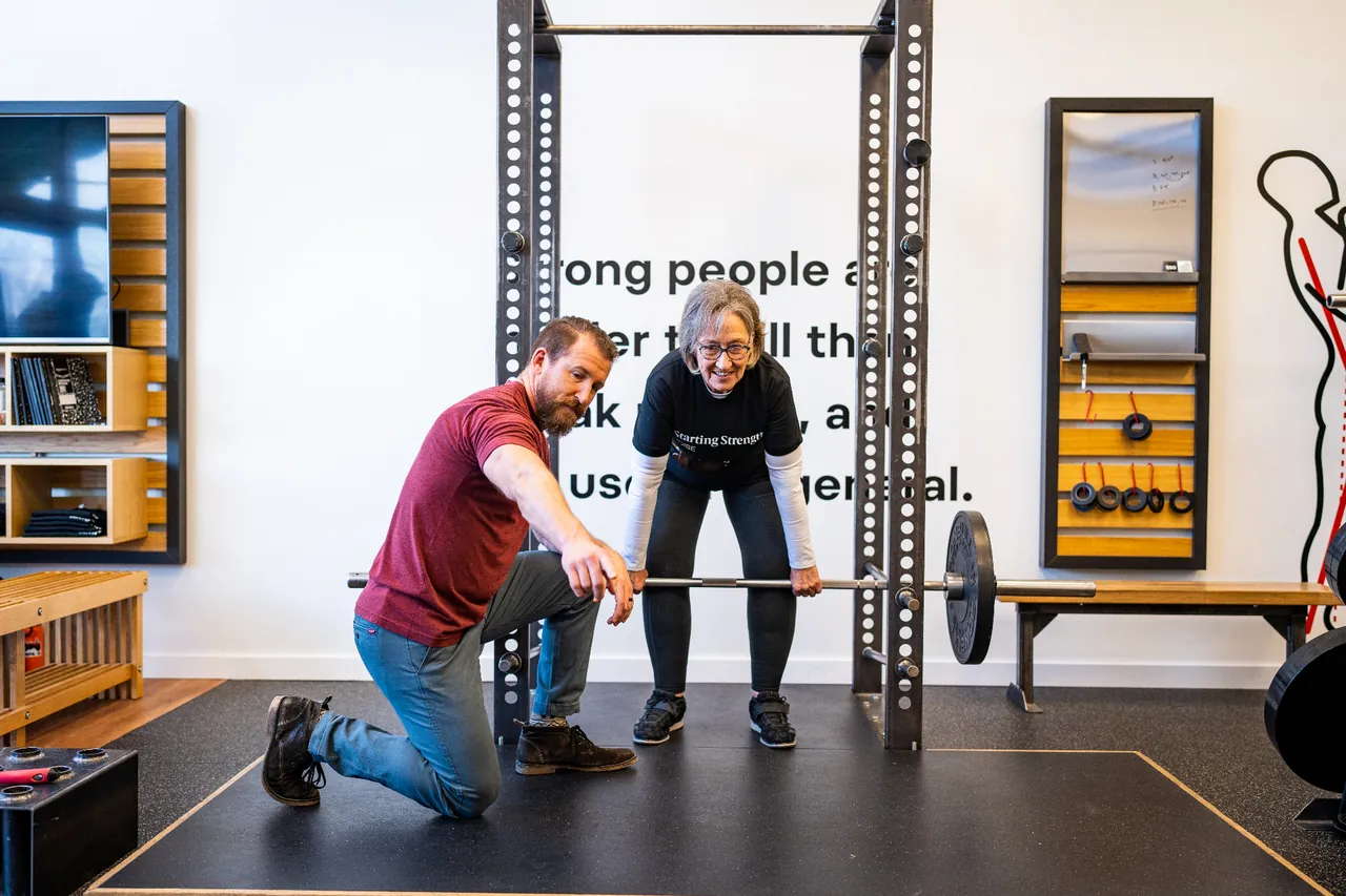 An older woman being coached through a deadlift at a Starting Strength gym