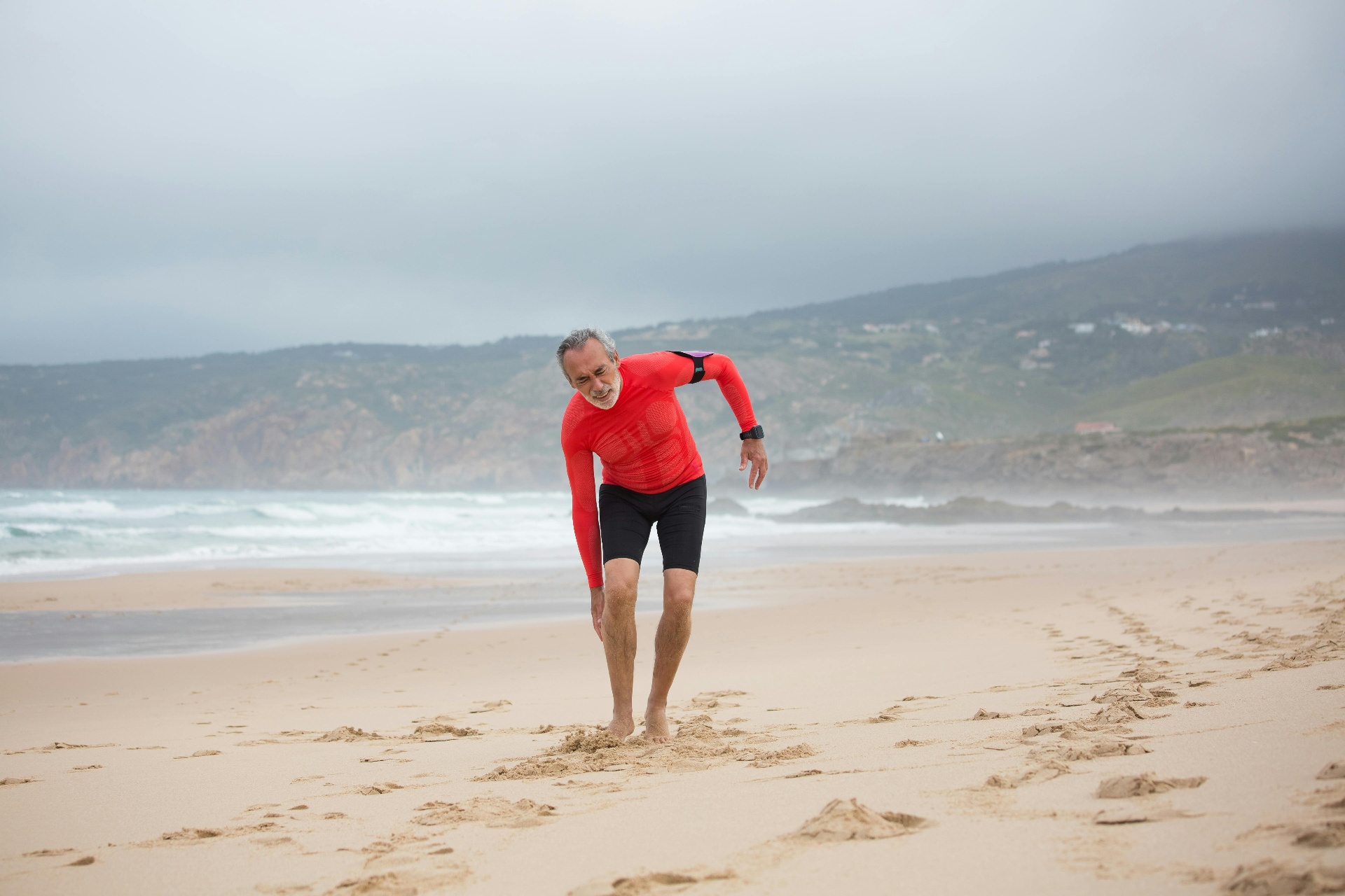 An older man struggling and out of breath while exercising on a beach