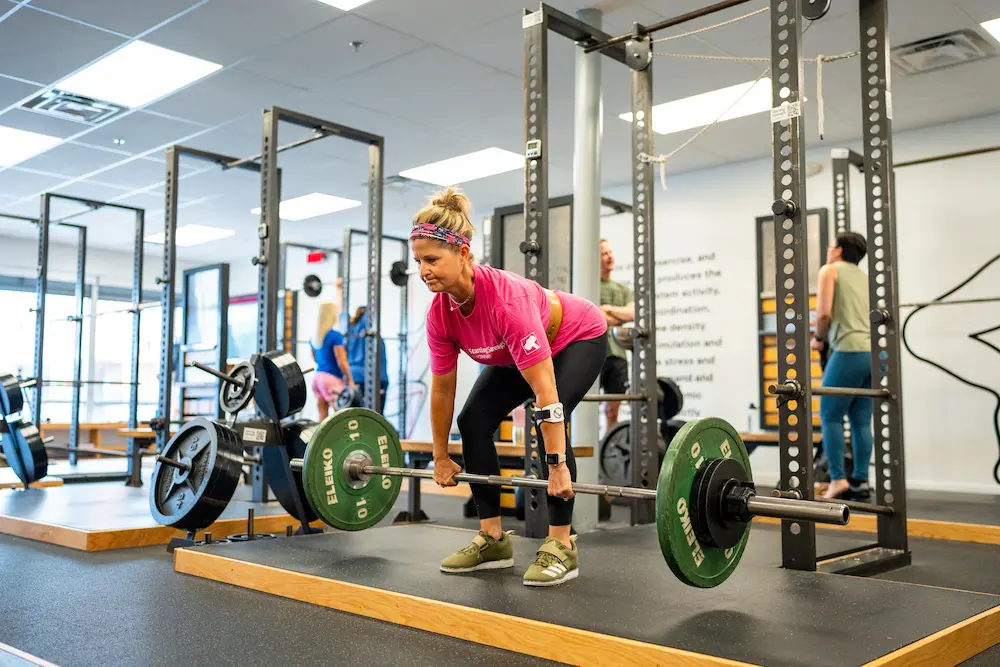 Female athlete in pink shirt performing deadlift with coaching supervision at Starting Strength gym