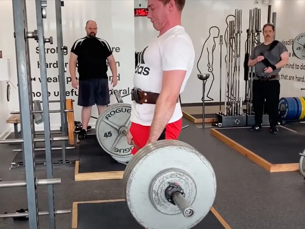 Male athlete Max performing deadlift in white shirt and red shorts