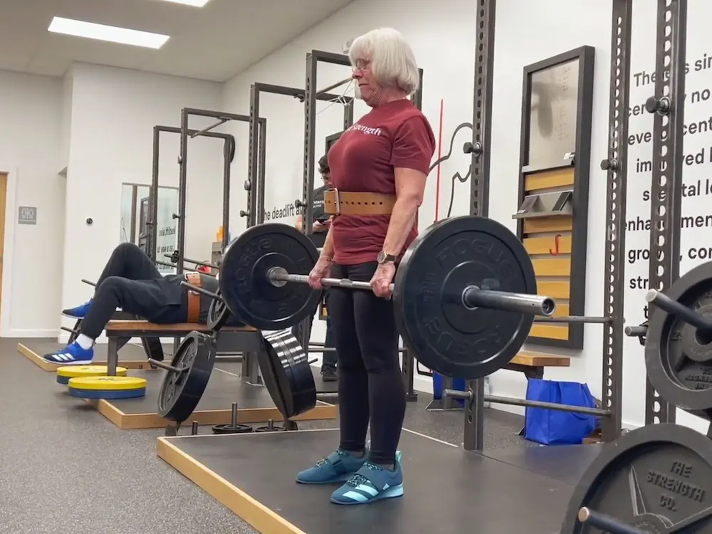 Senior female athlete performing deadlift with coaching assistance