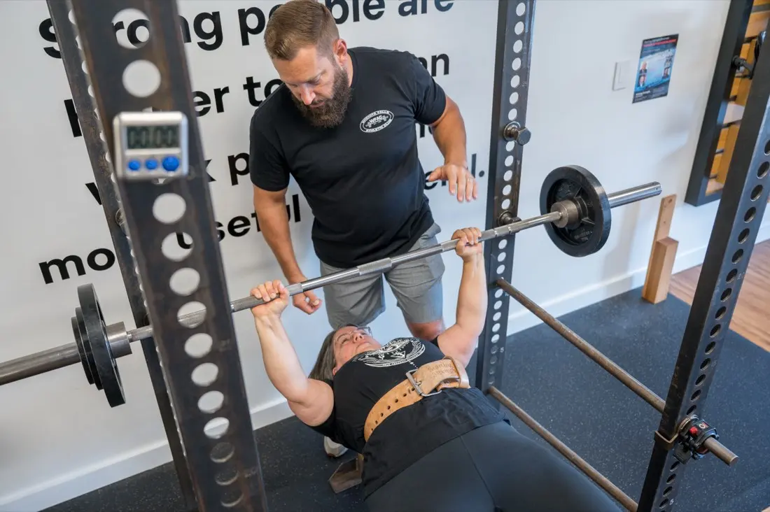 A coach guides a member through the bench press