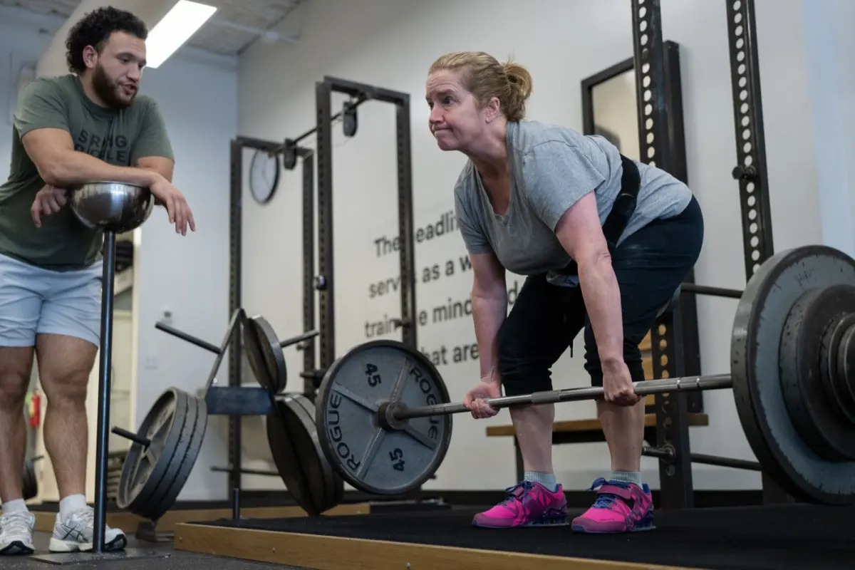 A member deadlifts while her coach watches her set closely