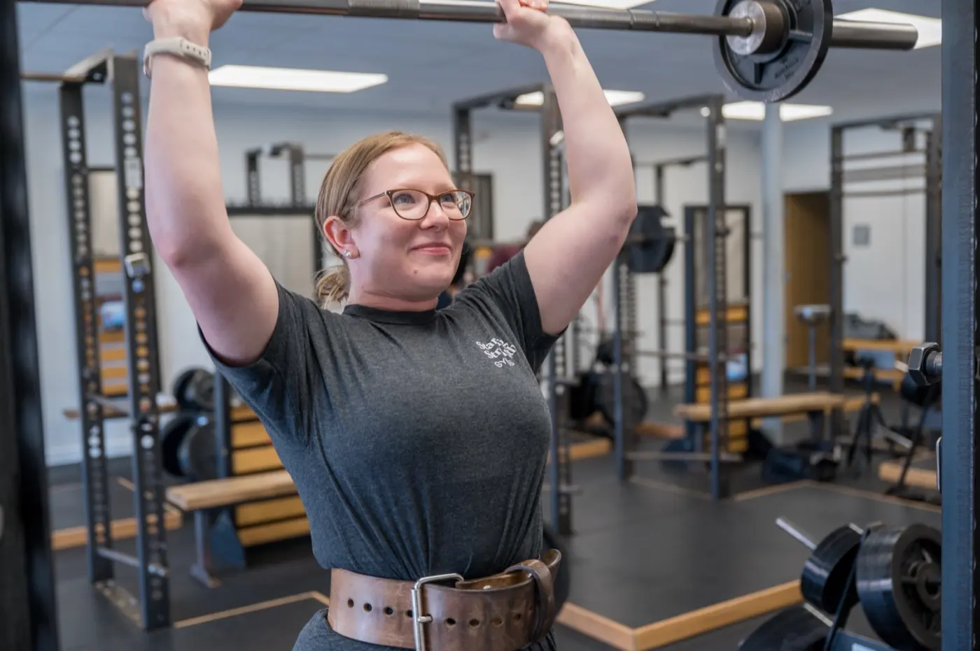 A smiling member presses a barbell overhead at Starting Strength Oklahoma City